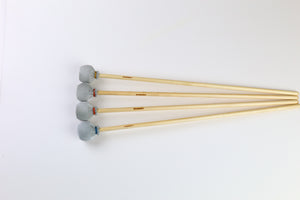 Four marimba mallets lined up in a row with grey heads and different colors of thread wrap.