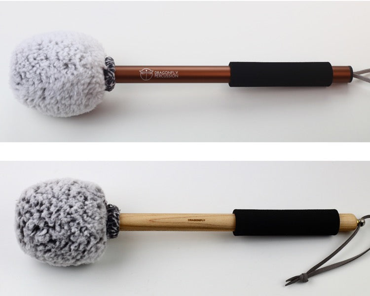 Fuzzbucket Gong mallets on two different handles.  Both mallets have a head wrapped in grey sherpa.  The top mallet has a bronze-colored aluminum handle and the bottom has a wooden handle.  Both have a black foam grip and strings for hanging.